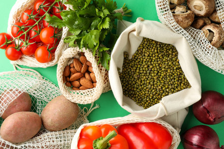 Eco bags with different food products on green background, flat lay