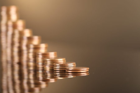 Stacks of coins on light brown mirror surface, closeup. Space for text