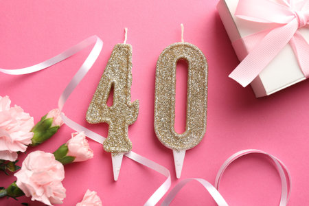 40th birthday. Number shaped candles, gift and flowers on pink background, flat layの写真素材