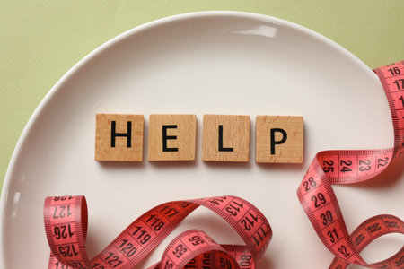 Bulimia. Plate with word Help and measuring tape on olive background, top view