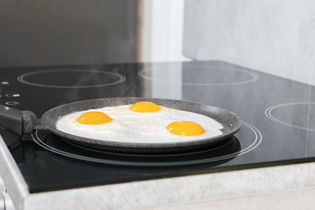 Cooking tasty eggs on frying pan in kitchen, closeupの写真素材