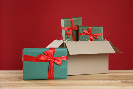 Parcel with gift boxes on wooden table against red background