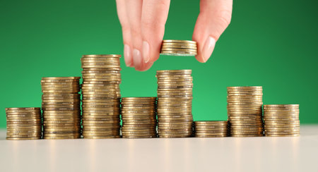 Woman putting coins onto stacks of ones at white table against green background, closeup