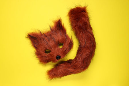 Fox mask and tail on yellow background, top view