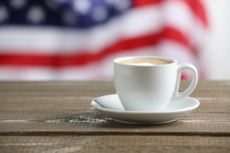 Aromatic coffee in cup on wooden table against flag of USA, space for textの写真素材