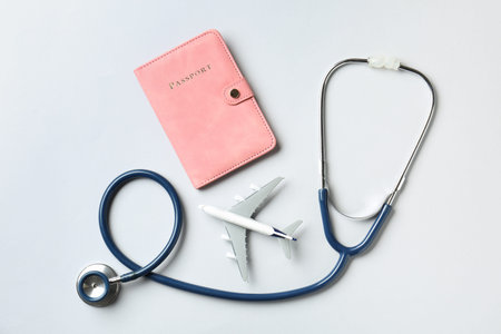 Medical tourism. Stethoscope, plane model and passport on light grey background, flat layの写真素材