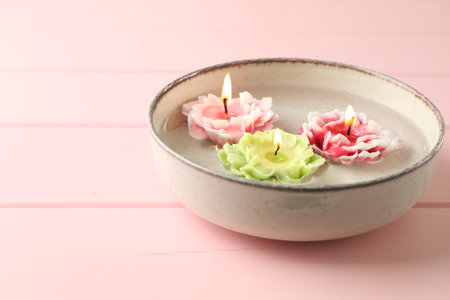 Beautiful burning flower shaped candles in dish with water on pink wooden table, closeup. Space for textの写真素材