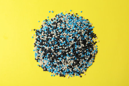 Pile of colorful plastic granules on yellow background, top viewの写真素材