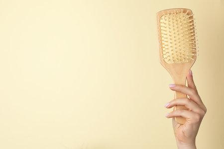 Woman with wooden brush on beige background, closeup. Space for textの写真素材