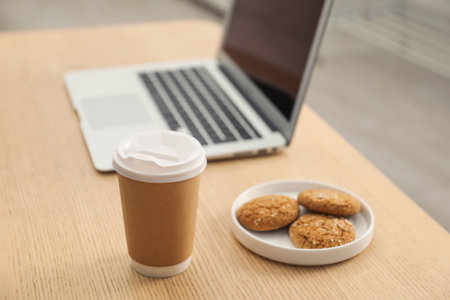 Paper cup, plate with cookies and laptop on wooden table indoors. Mockup for designの写真素材