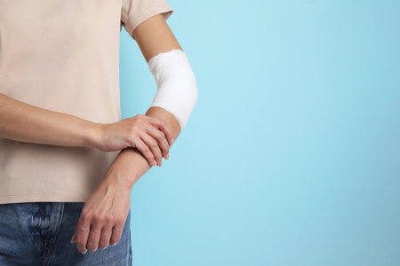 Woman with medical bandage on elbow against light blue background, closeup. Space for textの写真素材