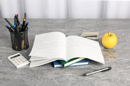 Doing homework. Notebook with math assignment and stationery on grey deskの写真素材