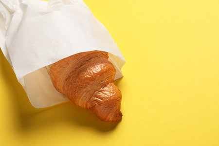 Paper bag with fresh croissant on yellow background, closeup. Space for textの写真素材