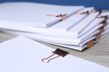 Binder clips with sheets of paper on wooden table, closeupの写真素材