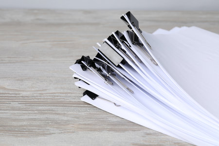 Binder clips with sheets of paper on wooden table, closeup. Space for textの写真素材