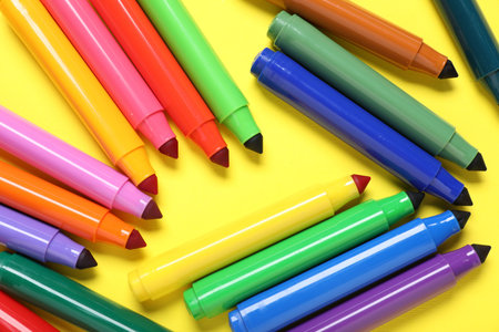 Many colorful markers on yellow background, flat lay
