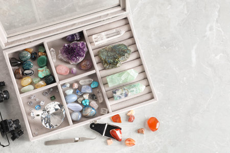 Box with beautiful gemstones and jeweler's tools on light table, flat lay