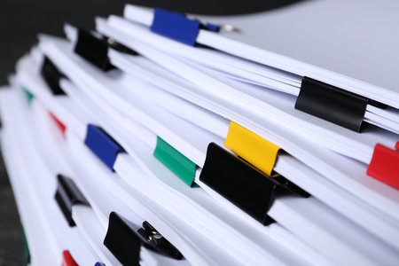 Colorful binder clips with sheets of paper on black background, closeup