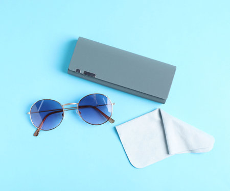 Case with stylish sunglasses and cleaning cloth on light blue background, flat layの写真素材