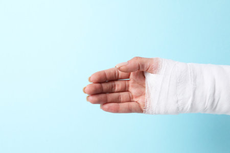 Woman with medical bandage on wrist against light blue background, closeup. Space for textの写真素材
