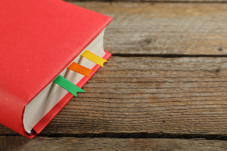Book with ribbon bookmarks on wooden table, closeup. Space for textの写真素材