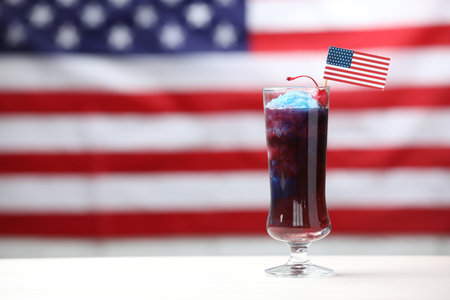 Tasty cocktail in glass with small paper flag of USA on white table against blurred background, space for textの写真素材