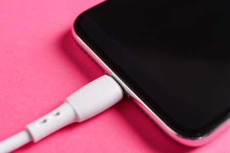 USB charge cable connected to smartphone on pink background, closeup