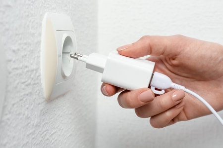 Woman plugging USB power adapter with charge cable into electrical socket indoors, closeup