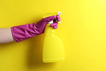 Woman with spray bottle of cleaning product on yellow background, closeup. Space for textの写真素材