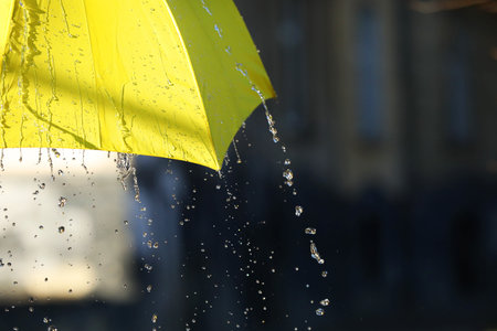 Open yellow umbrella under pouring rain outdoors, closeup. Space for text