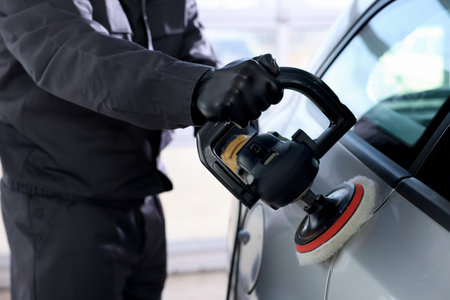 Man polishing car with orbital polisher indoors, closeup
