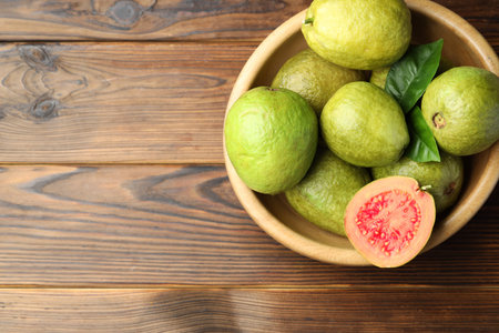 Fresh cut and whole guava fruits in bowl on wooden table, top view. Space for textの写真素材