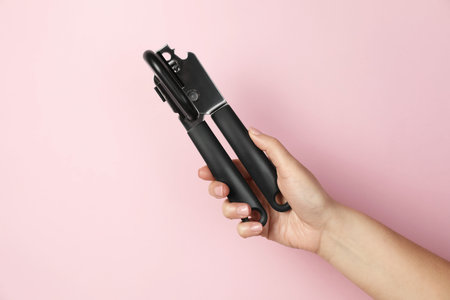 Woman holding can opener against pink background, closeupの写真素材