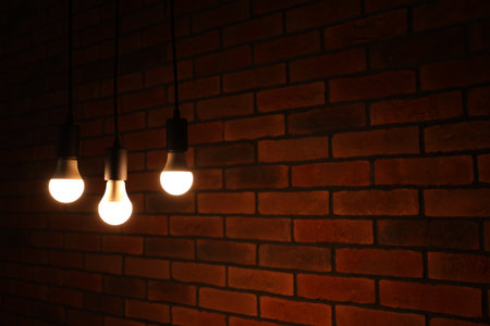 Glowing light bulbs hanging against brick wall, space for textの写真素材