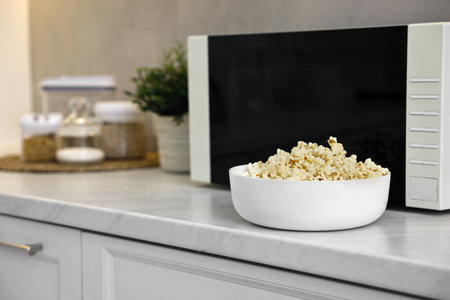 Bowl of popcorn near microwave oven on white marble countertop in kitchenの写真素材