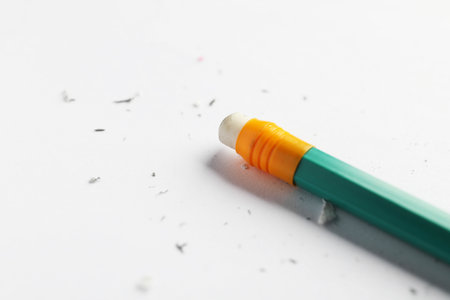 Pencil with eraser and scraps on white sheet of paper, closeup