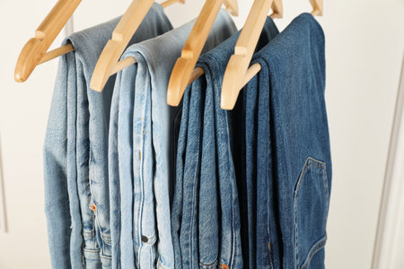 Many stylish jeans hanging against white wall, closeupの写真素材