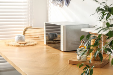 Closed microwave oven and kitchen utensils on wooden table indoorsの写真素材