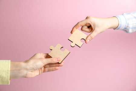 Business strategy and teamwork concept. Partners putting puzzle pieces together on pink background,...