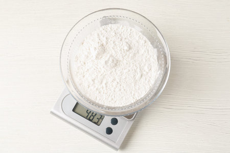Electronic kitchen scale with bowl of flour on white wooden table, top viewの写真素材