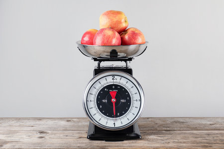 Mechanical kitchen scale with bowl of apples on wooden table against gray backgroundの写真素材