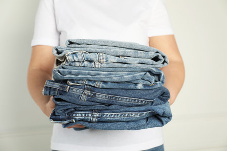 Woman with stack of different stylish jeans near light wall indoors, closeupの写真素材