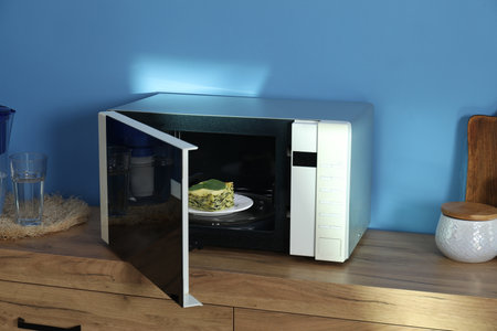 Open microwave oven with piece of lasagna on wooden cabinet indoorsの写真素材