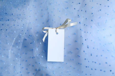 Blank tag with ribbon bow on white fabric, top viewの写真素材