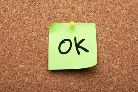 Paper note with abbreviation OK pinned to cork backgroundの写真素材