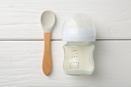 Feeding bottle with milk and spoon on white wooden table, flat layの写真素材