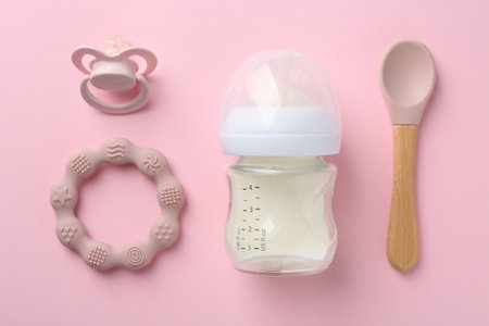 Feeding bottle with milk, spoon, pacifier and teether on pink background, flat layの写真素材