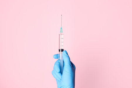 Doctor holding syringe with medication on pale pink background, closeupの写真素材