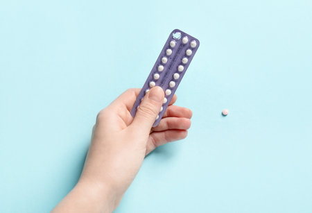 Woman holding blister of contraceptive pills on light blue background, closeupの写真素材