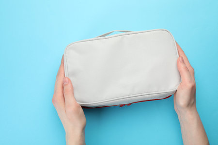 Woman with first aid kit on light blue background, top view